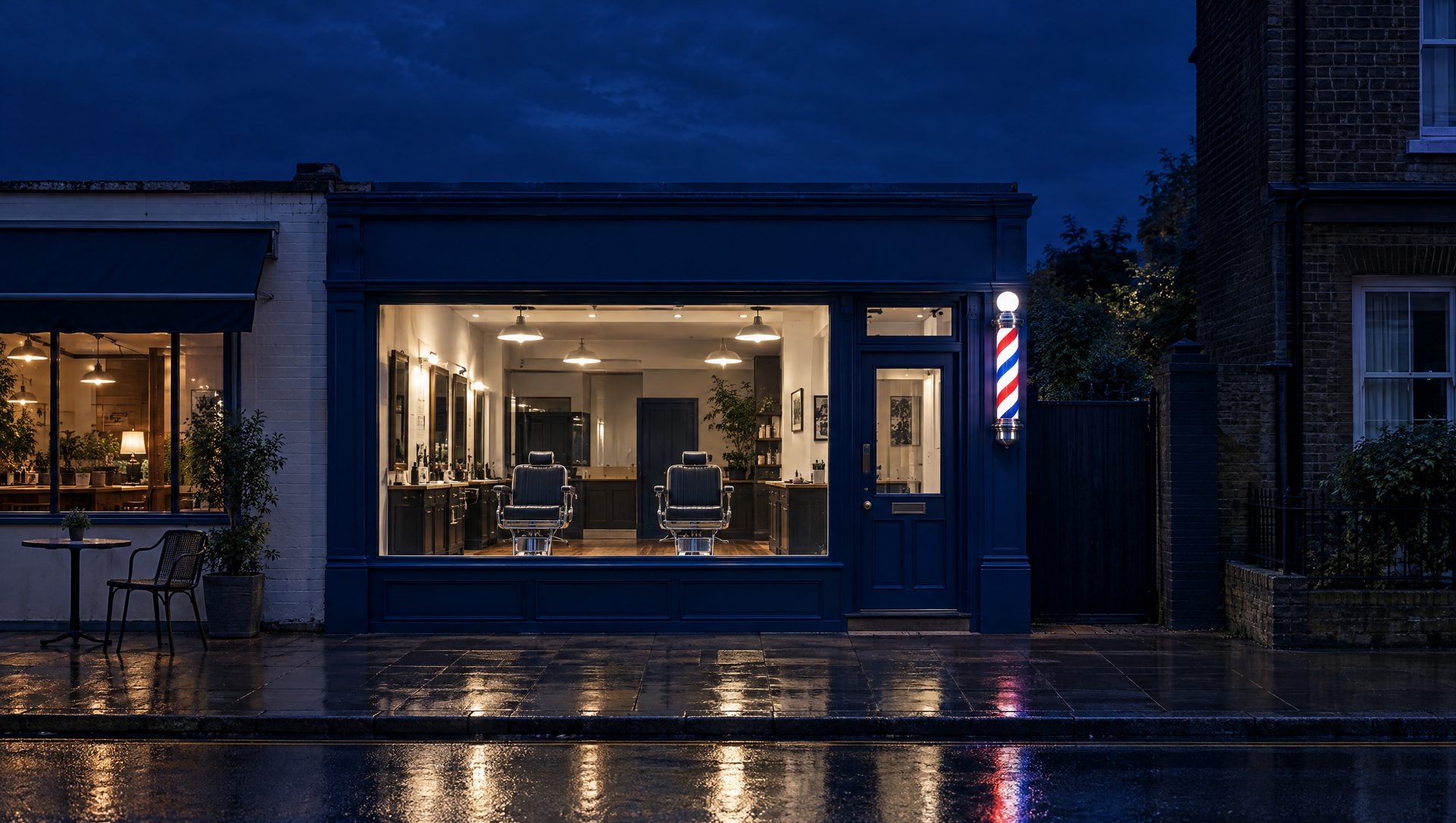 A navy-painted barbershop at dusk with a lit barber pole and two empty chairs in the window